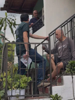 Alvarán entrega un volante a un vecino sentado en las escaleras de su casa, mientras otro escucha desde el balcón